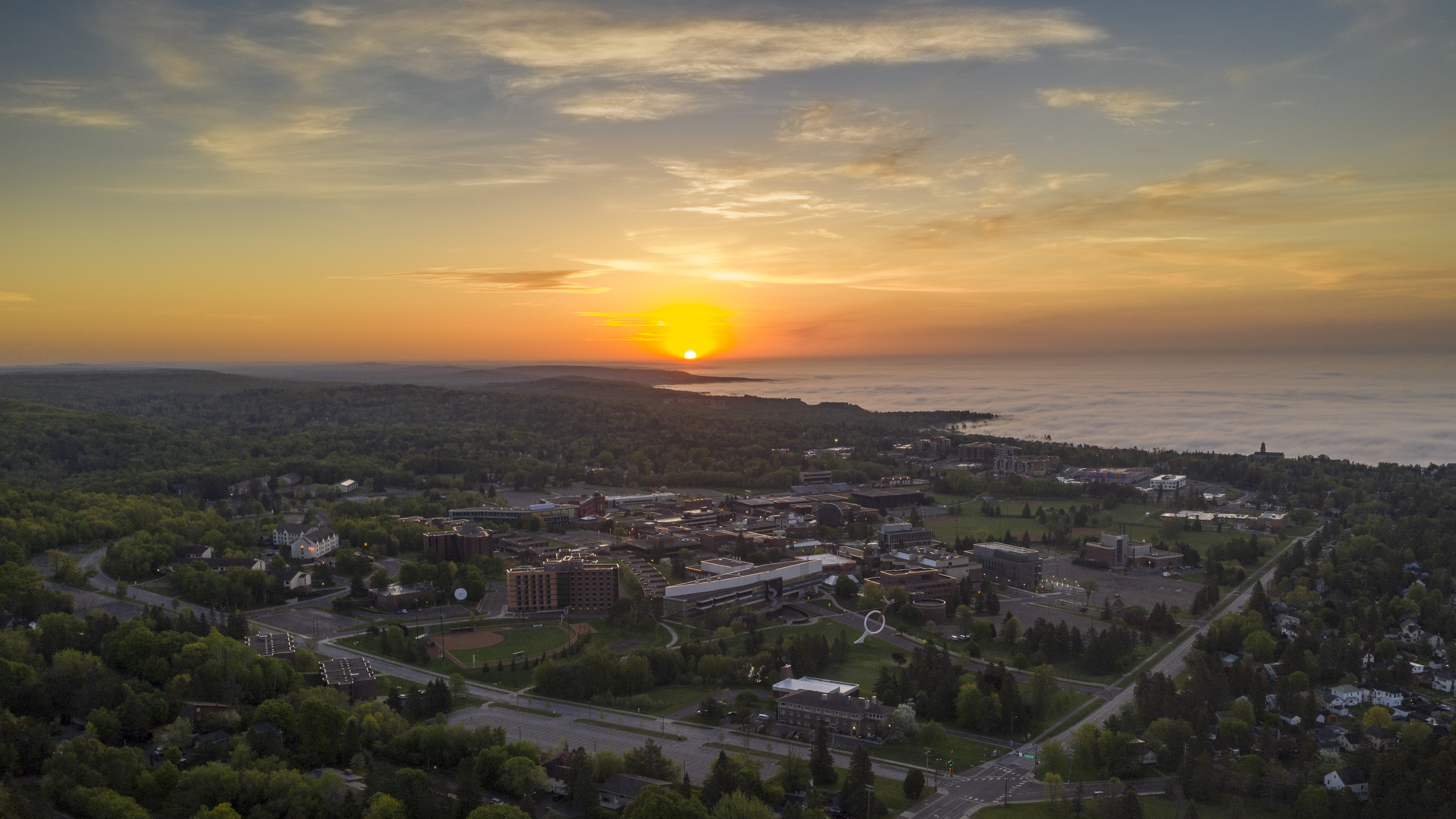 Aerial view of campus looking to the east as the sun rises over a foggy Lake Superior