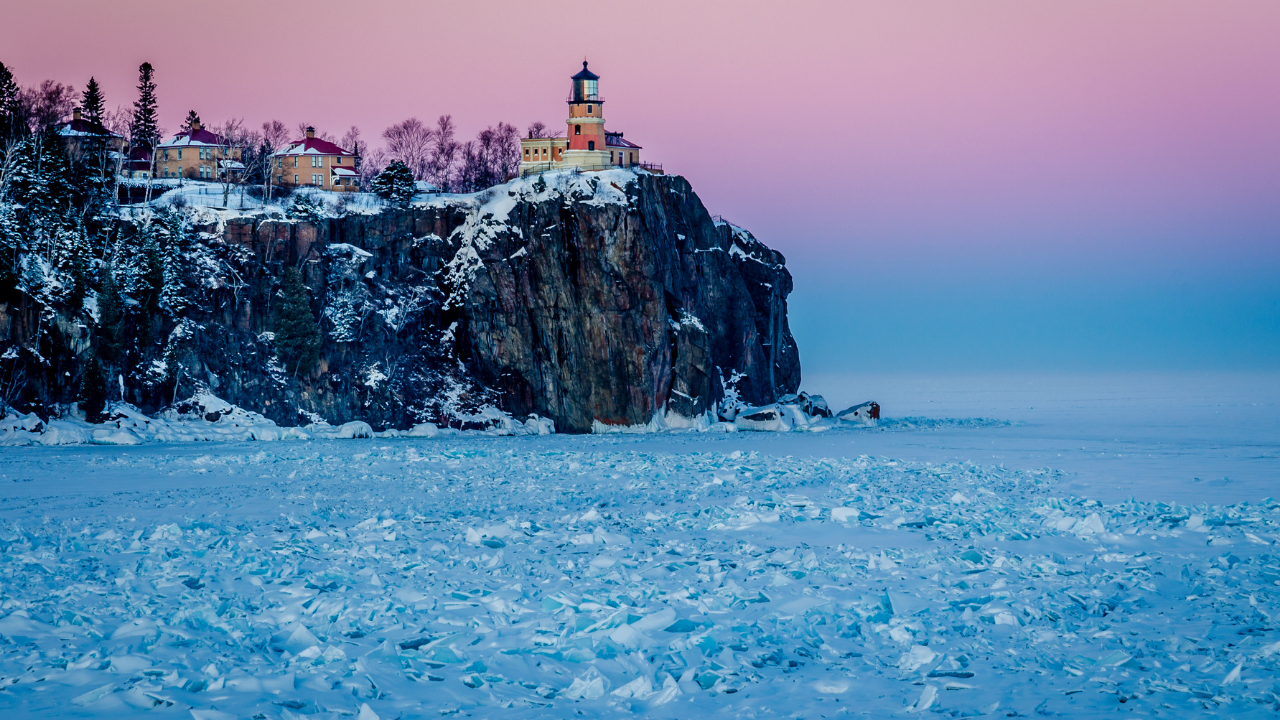 Split Rock Lighthouse above the frozen Lake Superior with a pink sunset.