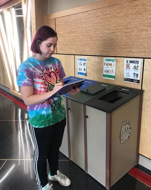 Student with clipboard and standing near waste sorting bins
